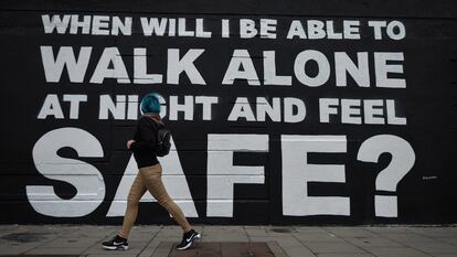 Una joven camina junto al último mural de la artista irlandesa Emmalene en el centro de Dublín en marzo de 2021. La inscripción dice: "¿Cuándo podré caminar sola por la noche y sentirme segura?".