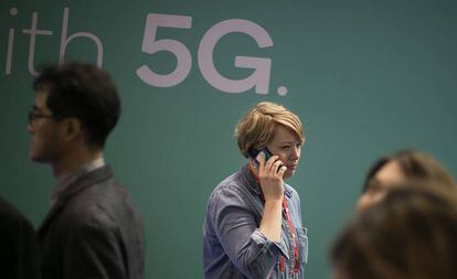 Una mujer camina mientras habla por telefono mientras pasa junto a un anuncio de tecnologia 5G.