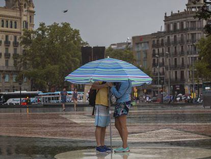 Una pareja bajo la lluvia y bajo una sombrilla en la plaza de Cataluña.
