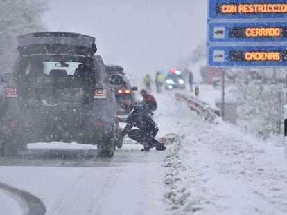 Varias personas ponen cadenas a los coches para poder circular por la carretera nevada, en Huesca este lunes.
