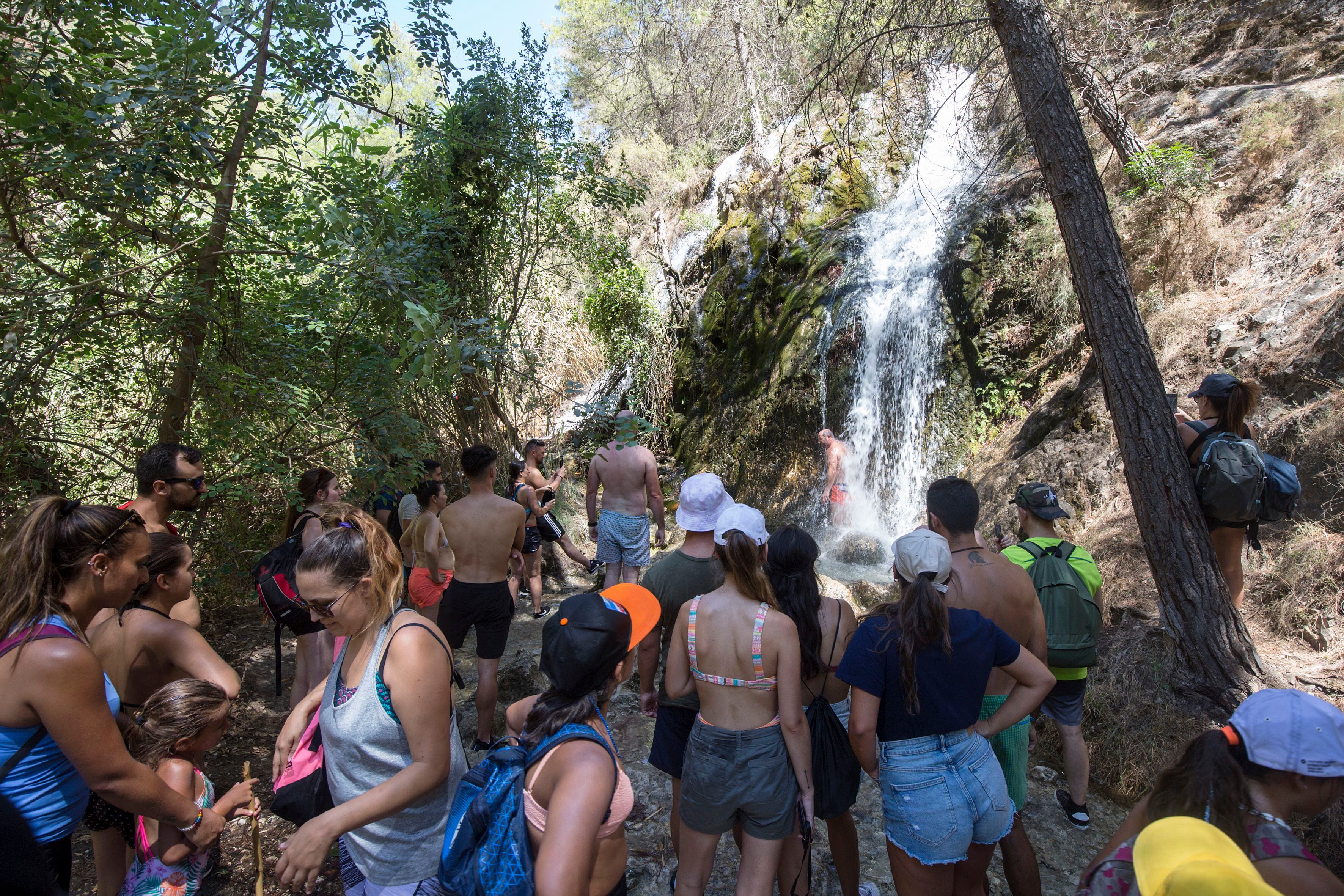 Varios turistas se amontonan delante de una cascada en el río Chíllar, en Nerja, Málaga.