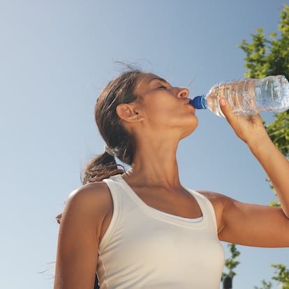 Una mujer bebe de una botella de agua de plástico.