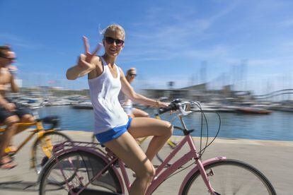 Una joven hace el gesto de la victoria mientras pasea en bicicleta por el paseo marítimo de Barcelona.