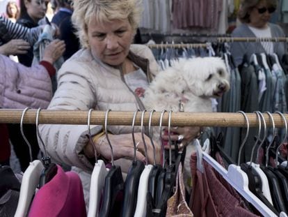 Una mujer ojea varias prendas con su perro en brazos en el mercadillo de Majadahonda.