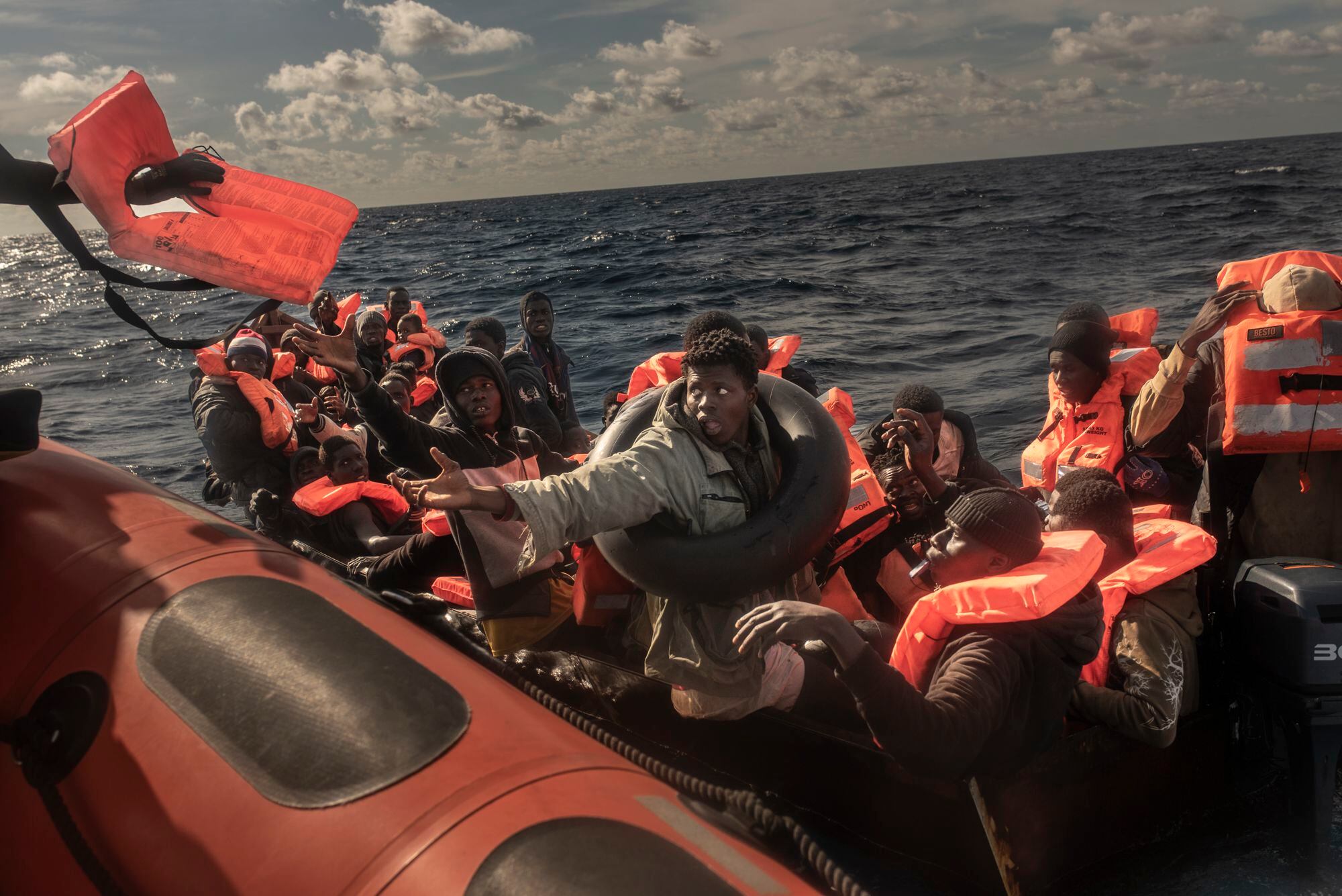 Un socorrista entrega un chaleco salvavidas a un joven migrante que viaja en la embarcación de hierro junto a otras 54 personas. El nerviosismo es palpable debido a las difíciles condiciones del mar, que dificultan el acercamiento de la lancha neumática de Open Arms.