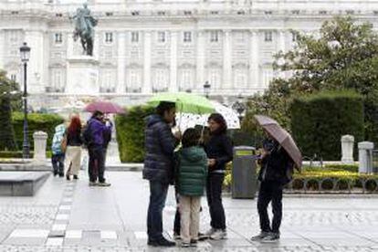 Un turista hace fotos, mientras que los miembros de una familia charlan bajo los paraguas y la lluvia en la Plaza de Oriente de Madrid. EFE/Archivo