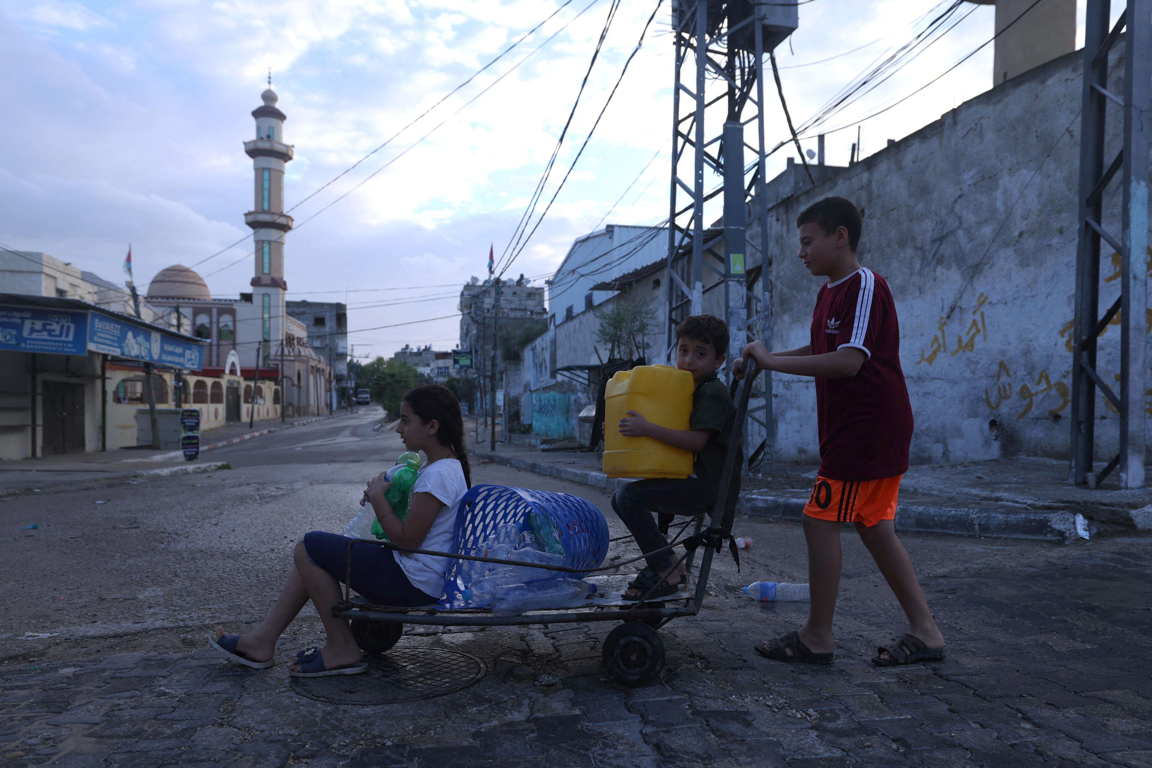 Tres niños palestinos buscan un lugar en el que rellenar garrafas de agua este martes en el campo de refugiados de Rafah, en el sur de Gaza.