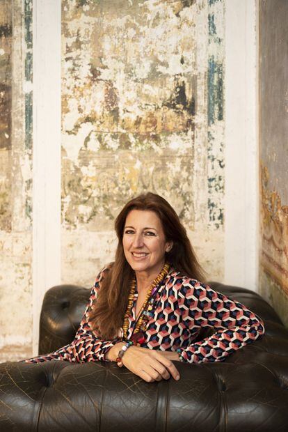 Benedetta Tagliabue, sentada en un sillón de piel tipo Chester frente a una pared con varias capas de pinturas decorativas de diferentes generaciones.