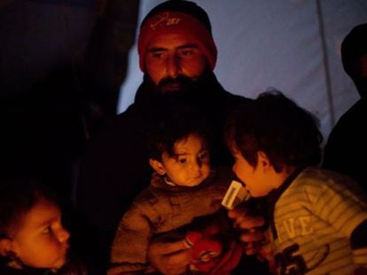 Un hombre se calienta junto a sus hijos en un campo de desplazados de la ciudad siria de Azaz, en el norte de la provincia de Alepo.