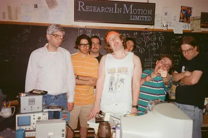 Imagen de la película 'BlackBerry', con los ingenieros que inventaron el aparato, liderados por Mike Lazaridus (encarnado por Jay Baruchel), a la izquierda, y Doug Fregin (Matt Johnson), con cinta en el pelo.
