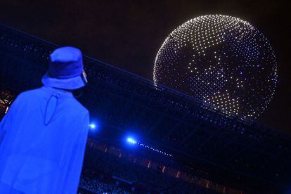 Un voluntario observa el vuelo de varios drones formando un globo terráqueo en el cielo del Estadio Olímpico, durante la ceremonia de apertura de los Juegos Olímpicos de Tokio 2020.