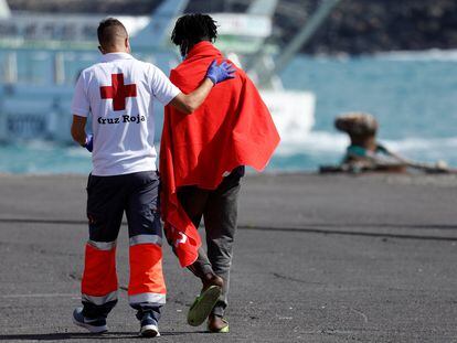 Un voluntario de la Cruz Roja acompaña a un inmigrante en el puerto de Arguineguin (Gran Canaria) después de que la embarcación en la que viajaba fuera rescatada por la guarda costera española.