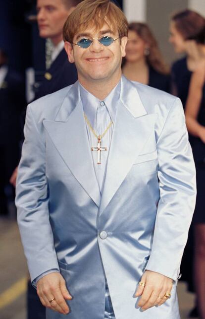 <p><strong>Cuándo.</strong> En una fiesta de Versace en Londres en 1995.</p> <p><strong>Por qué.</strong> Porque Elton John siempre ha sido un pionero a la hora de lucir prendas, colores y accesorios que pocos hombres se atrevían a llevar en público. Con Elton llegaron el color, los acabados satinados, la joyería y el barroquismo a las alfombras rojas. No en vano fue el mejor cliente de Gianni Versace, que solía decir que los armarios del inglés custodiaban un archivo de prendas de Versace más completo que el de su propia firma. Aquí declinó en clave monocroma un color poco habitual (un azul pastel casi violeta) con un corte retro (fíjese en esas solapas en pico que siguen en los setenta) y una sana dosis de joyería tan ostentosa que parece bisutería. El cielo es de los valientes.</p>