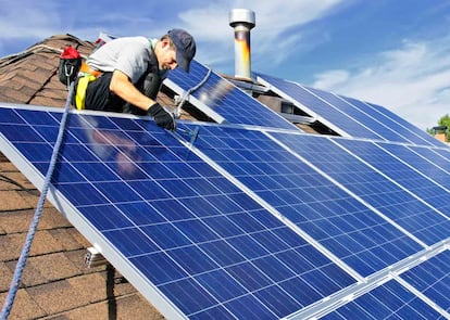 Un operario instala paneles solares en el tejado de una casa.