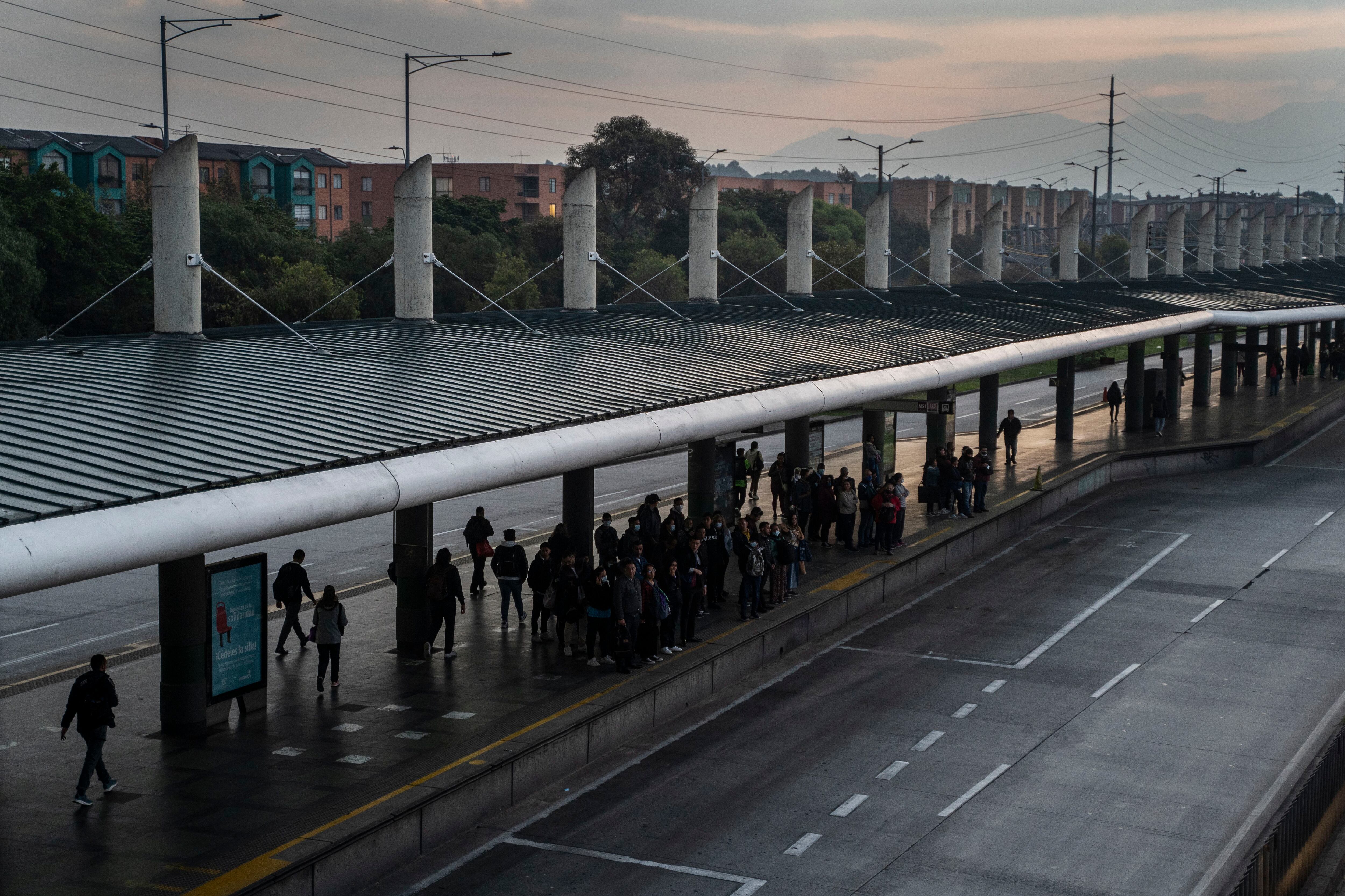 Los usuarios hacen fila para abordar el transporte público al amanecer en Bogotá. 