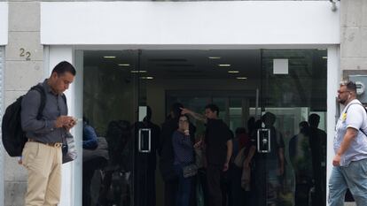Usuarios frente a una sucursal de BBVA en Ciudad de México que revisan su celular y hacen operaciones bancarias.