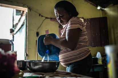 Yaquelín en el interior de su casa, con las garrafas de agua potable que debe transportar desde lo algo para poder cocinar y beber. Barrio de Simón Bolívar, en Santo Domingo.