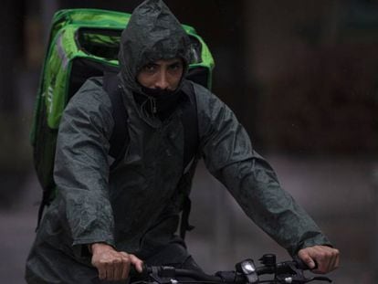 Un 'rider' (repartidor) trabaja bajo la lluvia protegido con un impermeable, en Sevilla.