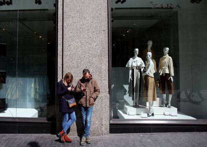 Un hombre y una mujer miran su móvil a las puertas de una tienda de Zara en Madrid