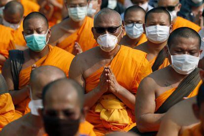 Varios monjes budistas del templo Dhammakaya cubren sus rostros mientras corean consignas durante un enfrentamiento con la policía a las puertas del templo en la provincia de Pathum Thani, a las afueras de Bangkok (Tailandia).