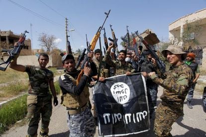 Un grupo de soldados y paramilitares sostiene una bandera del Estado Isl&aacute;mico arrebatada a los yihadistas durante la ofensiva de Tikrit.