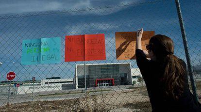 Una mujer participante en una protesta por la reclusi&oacute;n de 600 migrantes en el Centro Penitenciario Archidona II pega carteles reivindicativos en la valla del recinto.