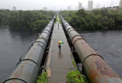 Varias personas caminan sobre tuberías para cruzar el 'Mahim Creek' durante las lluvias de Bombay, India.