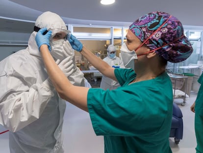 Una enfermera de la unidad de cuidados intensivos (UCI), ayuda a un compañero a colocarse las protecciones necesarias antes de entrar en un box para atender a un paciente infectado con COVID 19, en el hospital universitario Morales Meseguer de Murcia.