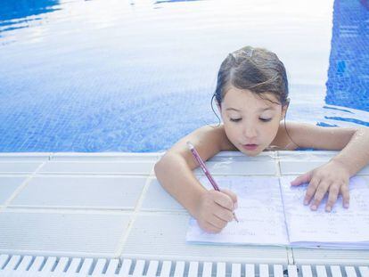 Una niña haciendo deberes en la piscina.