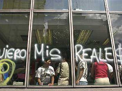 Un grupo de personas espera en un banco de Caracas, tras una pintada que exige poder retirar el dinero.