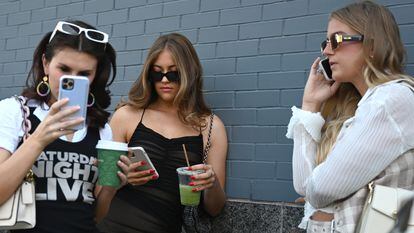 Tres jóvenes usan sus teléfonos móviles a las puertas de un desfile de la Semana de la Moda de Nueva York de 2022.