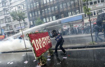 Un policía turco retira un letrero del Primero de Mayo colocado en una calle de Estambul mientras sus compañeros disparan cañones de agua para disolver la manifestación.