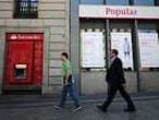 Dos viandantes pasan frente a una sucursal del Banco Santander y una del Banco Popular en Madrid