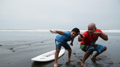 Surfing instructor Ernesto Soriano and Mariano Pineda, a child, prepare to ride waves as they participate in the Surftismo program, an alternative therapy for children with autism spectrum disorder diagnoses that uses surfing, in Chiltiupan, El Salvador August 14, 2022. REUTERS/Jose Cabezas