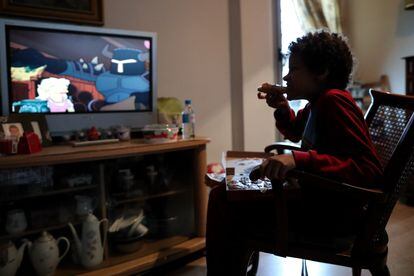 Un niño come un trozo de pizza del menú infantil de Telepizza mientras ve la televisión en su casa, en Usera.