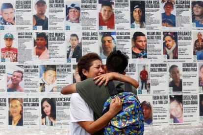 Una mujer abraza a su hijo frente a un mural con información de personas desaparecidas en México