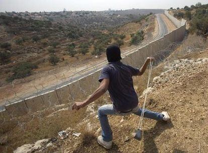 Un palestino lanza una piedra contra una patrulla israelí al otro lado del muro, cerca de Ramala.