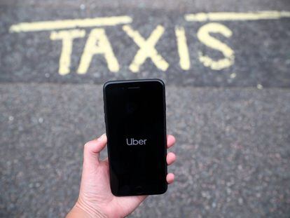Una persona sostiene un m&oacute;vil con la aplicaci&oacute;n de Uber frente a una parada de taxis. 