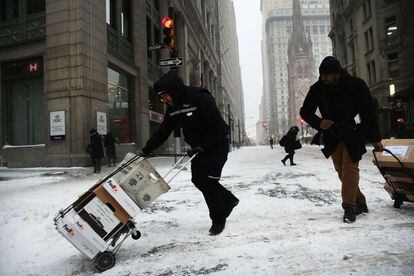Trabajadores del servicio postal empujan sus carros por una calle cubierta de nieve.