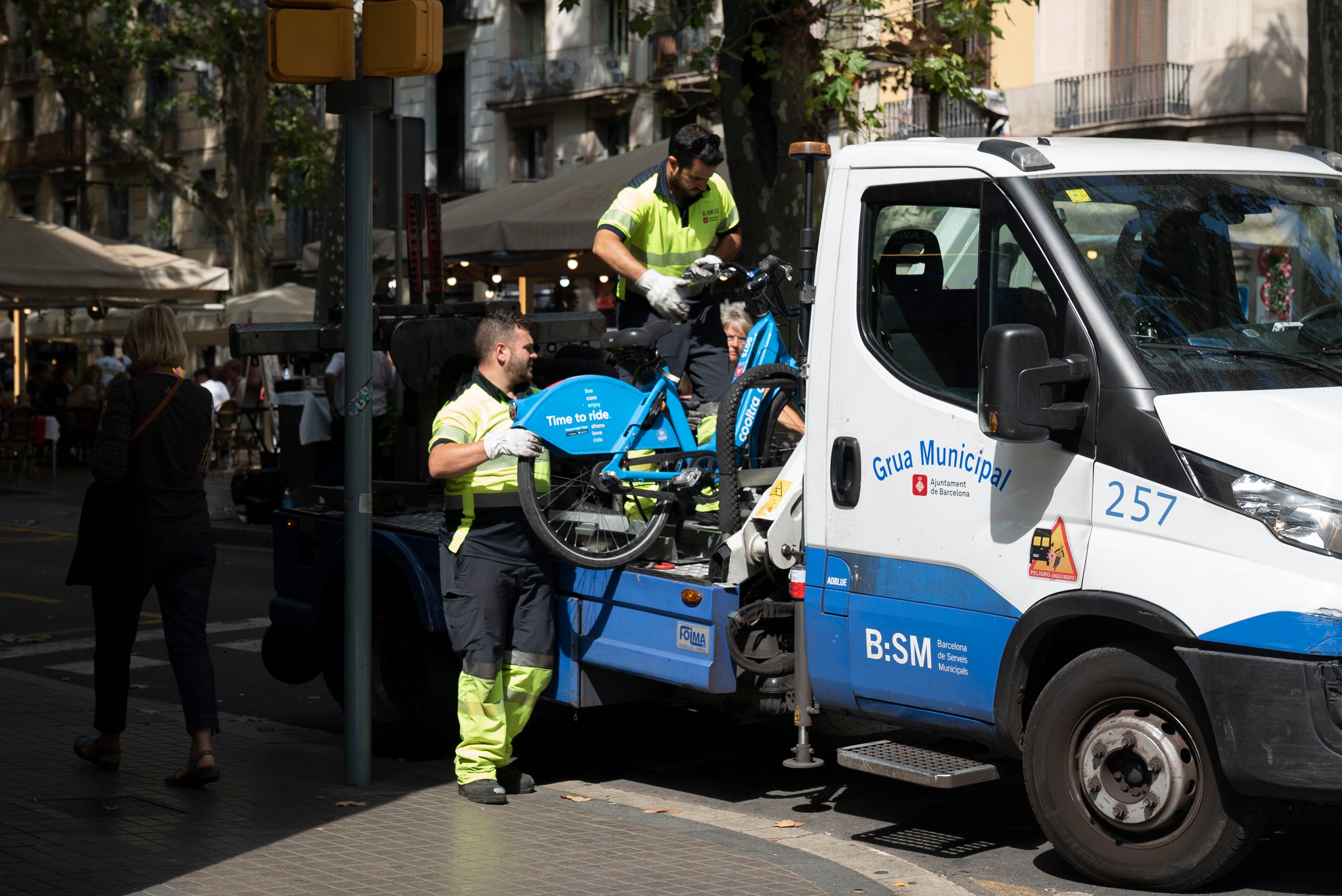 Operarios de la grúa municipal de Barcelona se llevan bicicletas de alquiler mal aparcadas, en septiembre. 